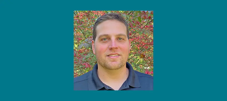 Pictured: Dan Clemson posing in front of foliage while wearing a blue polo.
